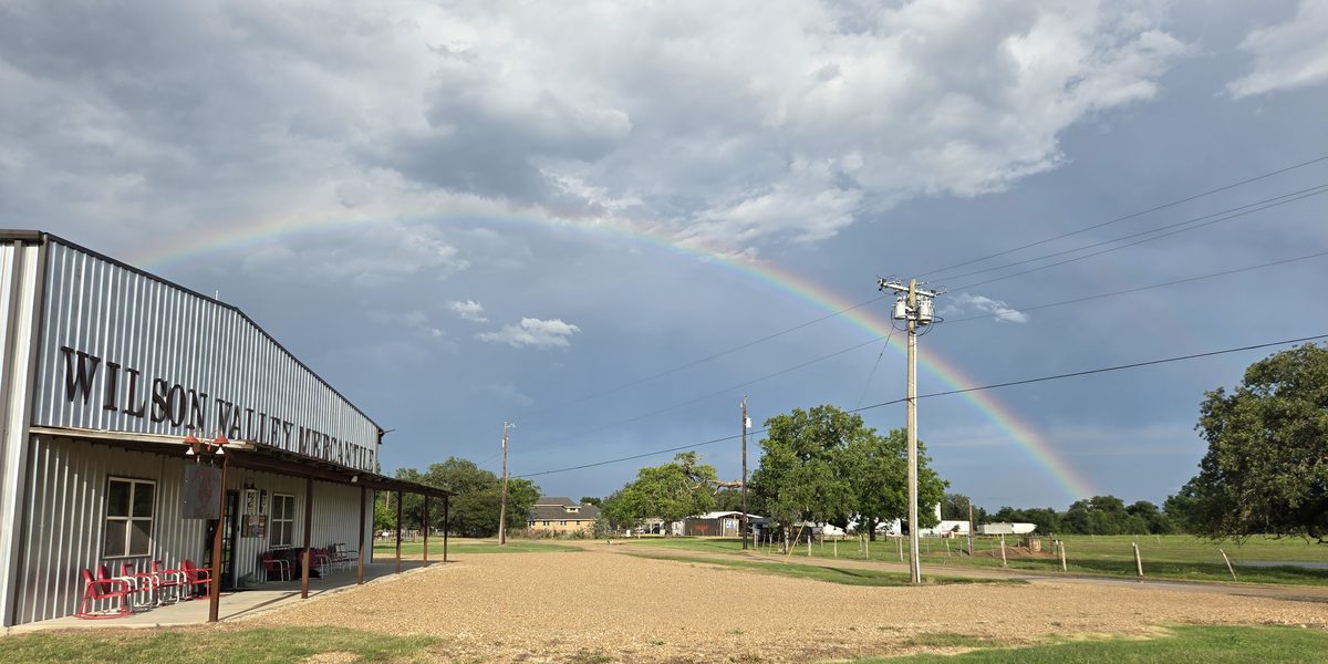 The Wilson Valley Mercantile building under a full rainbow, seen from across the gravel lot as a storm clears